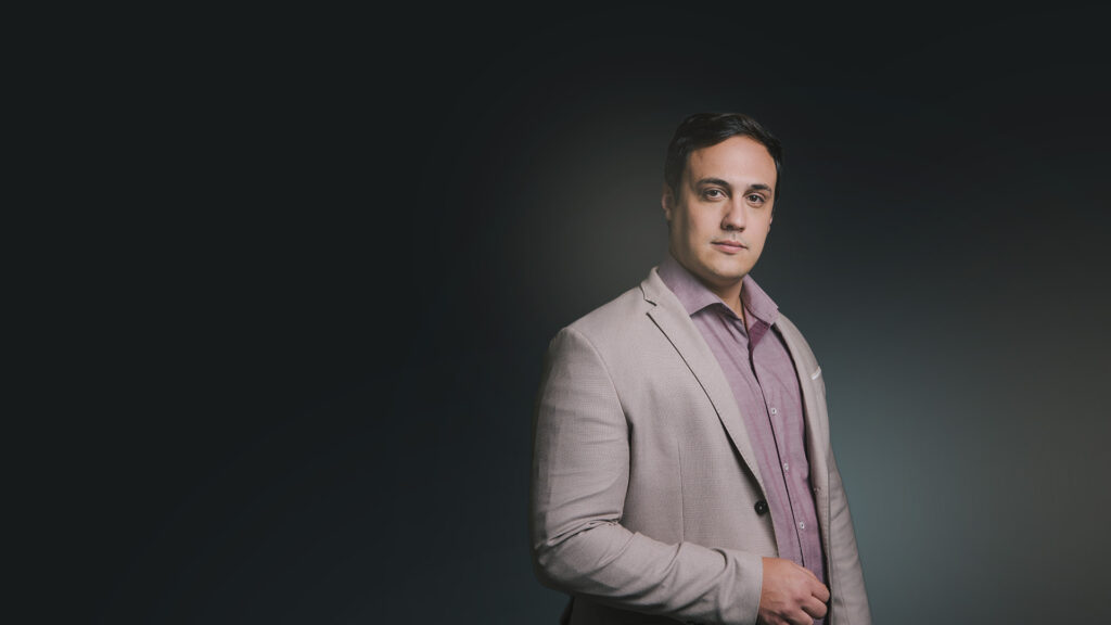 Lucas Naves de terno claro diante de fundo escuro.